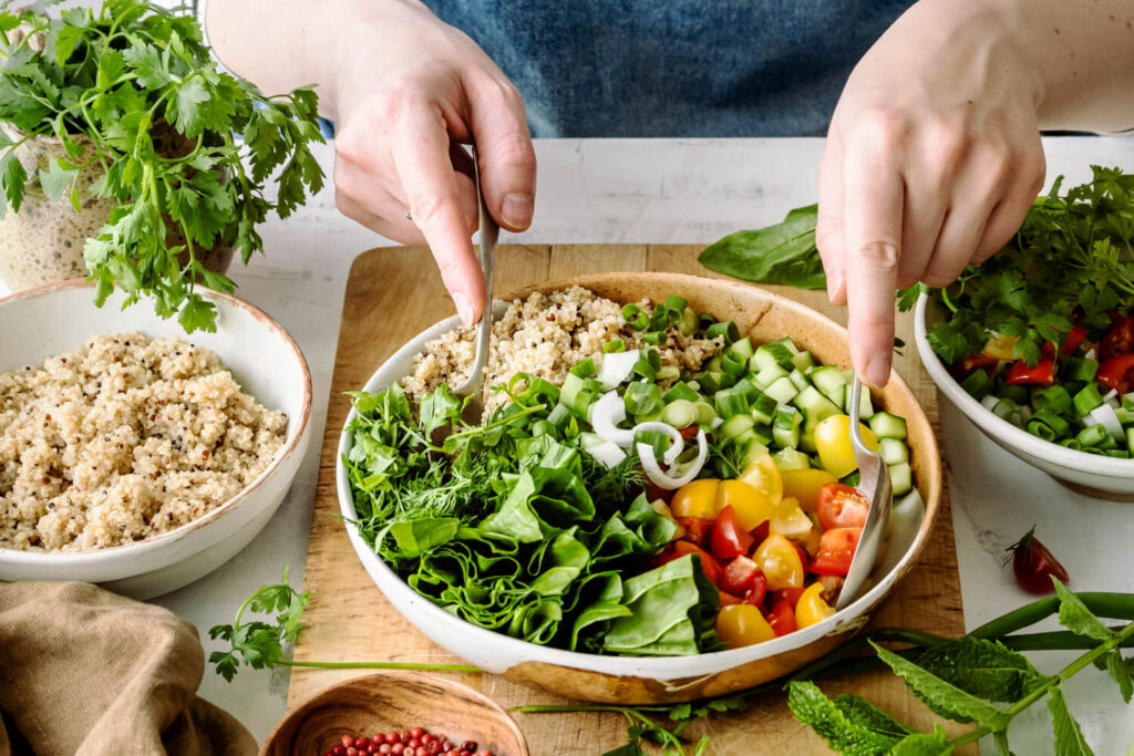 Pessoa preparando uma refeição saudável com salada colorida, vegetais frescos e grãos, em um ambiente claro e organizado, transmitindo a ideia de alimentação leve e equilibrada que contribui para uma melhor qualidade do sono.