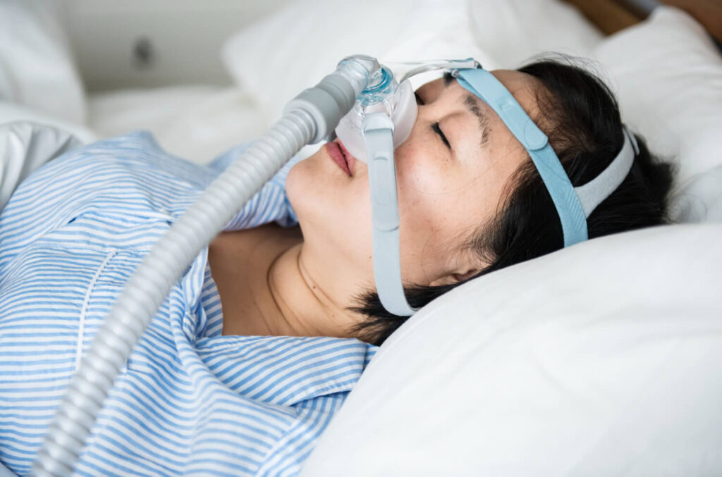 Mulher dormindo com aparelho CPAP para tratamento da apneia do sono, condição que pode agravar a privação do sono e comprometer a qualidade do descanso.